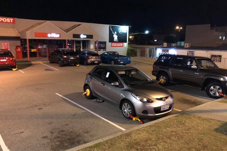 A car park showing several cars with wheel clamps attached.