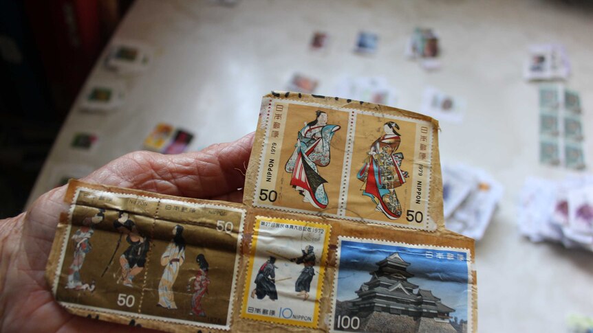 Lyn Saul holding up a large panel of international stamps sent from Japan.