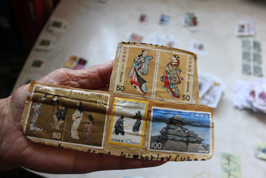 Lyn Saul holding up a large panel of international stamps sent from Japan.