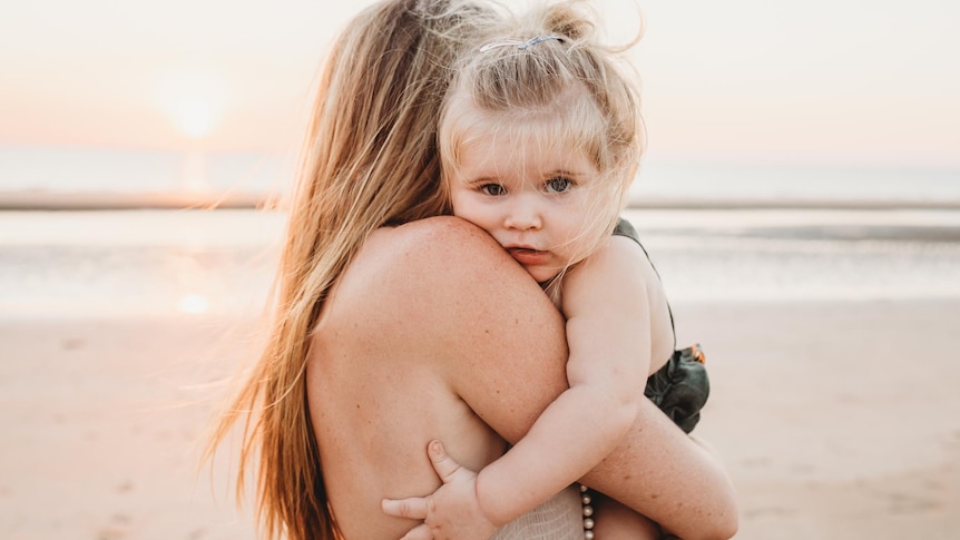 mother holding her daughter at the beach, the sun is setting behind them