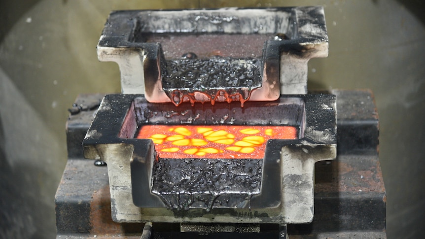 Two stacked metal dishes with silvery sludge spilling out, the bottom one has a glowing, bright orange liquid
