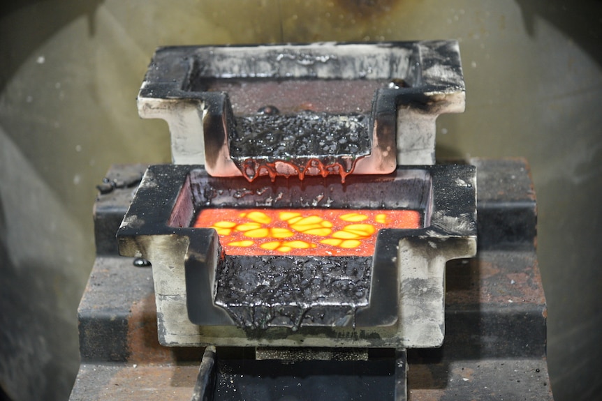 Two stacked metal dishes with silvery sludge spilling out, the bottom one has a glowing, bright orange liquid