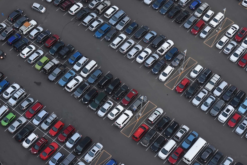 A picture taken from above of rows of vehicles parked in a bitumen carpark.