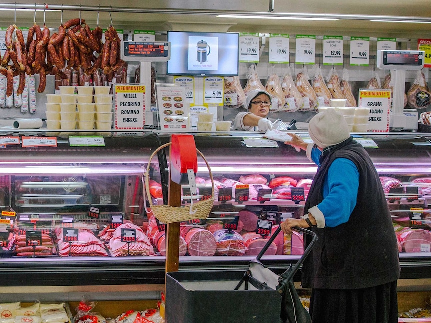 Un cliente habitual que empuja un carrito de la compra de cuero es atendido en la charcutería.