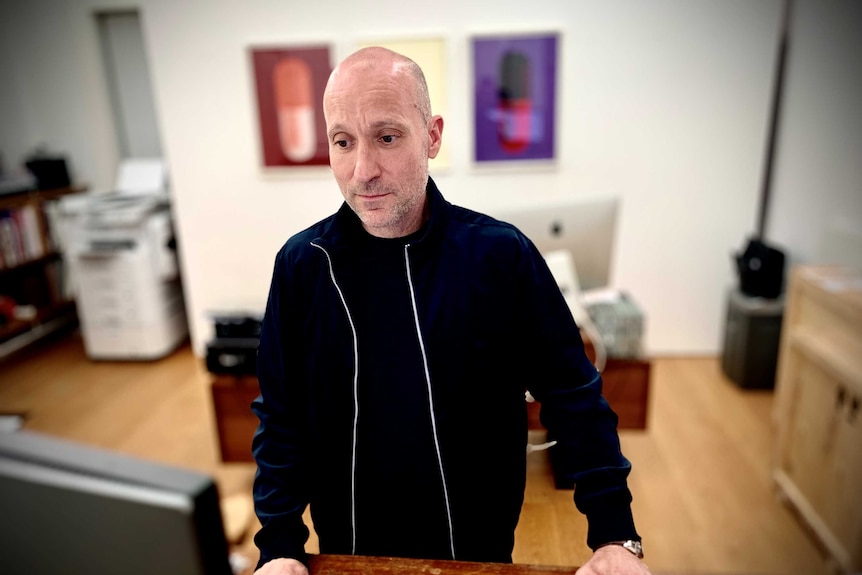 A man stands at a desk looking at a computer screen.