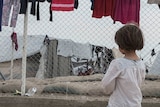 A little girl looks through a barb wire fence at the camp.