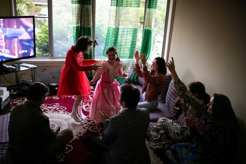 Two young girls dancing while a family watch on.