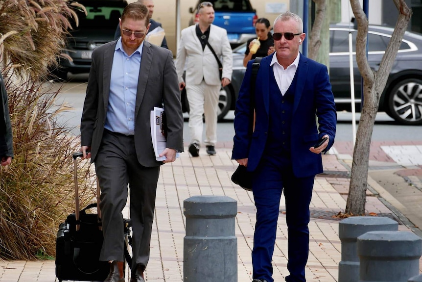 Two men in suits walking along a footpath outside a court building.
