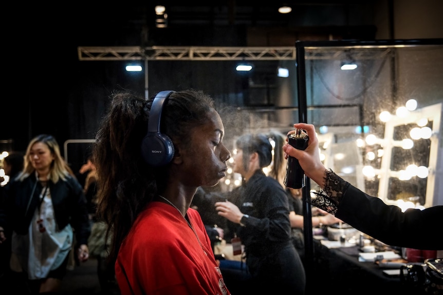 a young model gets a spray on her face as she get ready to model clothing 