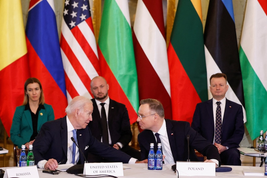 Biden and Duda lean in as they speak, Biden's hand on his arm. Displayed behind them are the B9 and US flags