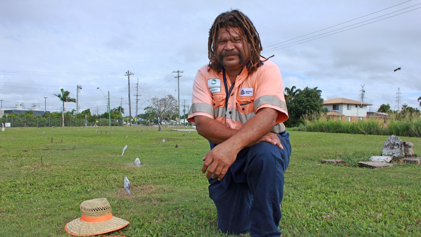 Man with dreadlocks sitting on the grass surrounded by pegs parking graves