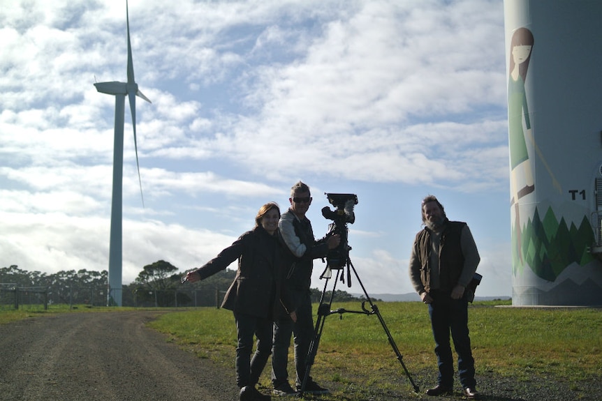 Crew standing next to wind turbine and painted wheat silo.