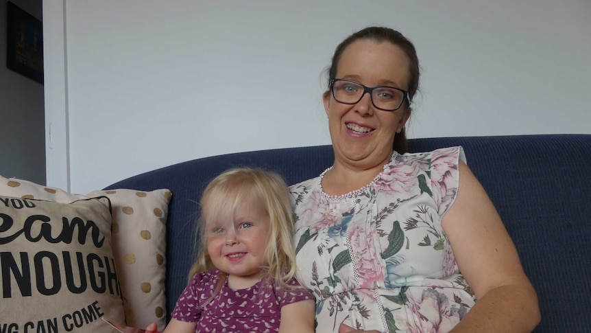 A woman sits on a couch with her young daughter.