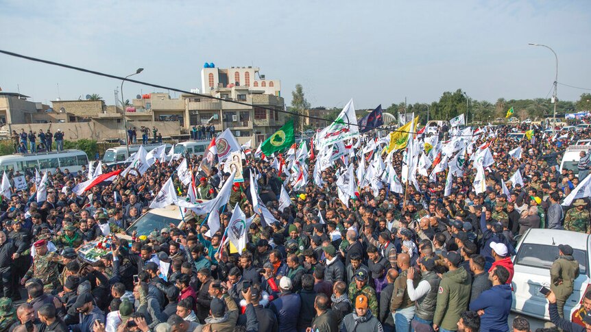 A street in Bagdad is blanketed by a funeral procession on a clear day as people carry various flags.