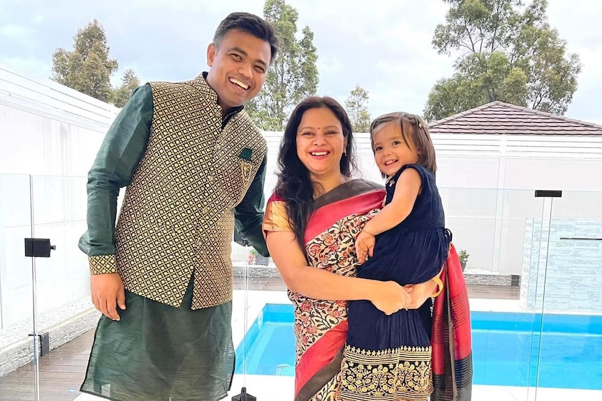 A South Asian couple dressed in traditional Indian clothing holding up a child