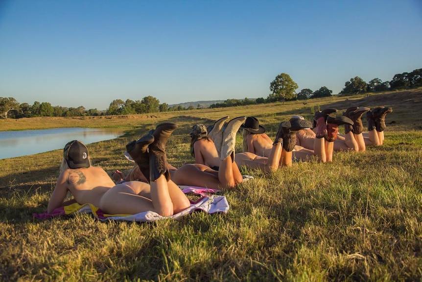 Six women lying naked on grass next to dam in regional QLD