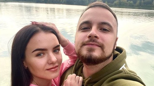 A woman and man take a selfie in front of a lake. 