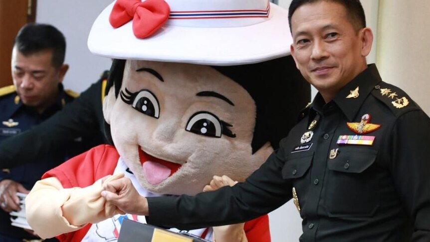 A uniformed solider links his pinky with a reconciliation mascot - a cartoon girl with a red love heart on her white dress.