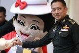 A uniformed solider links his pinky with a reconciliation mascot - a cartoon girl with a red love heart on her white dress.