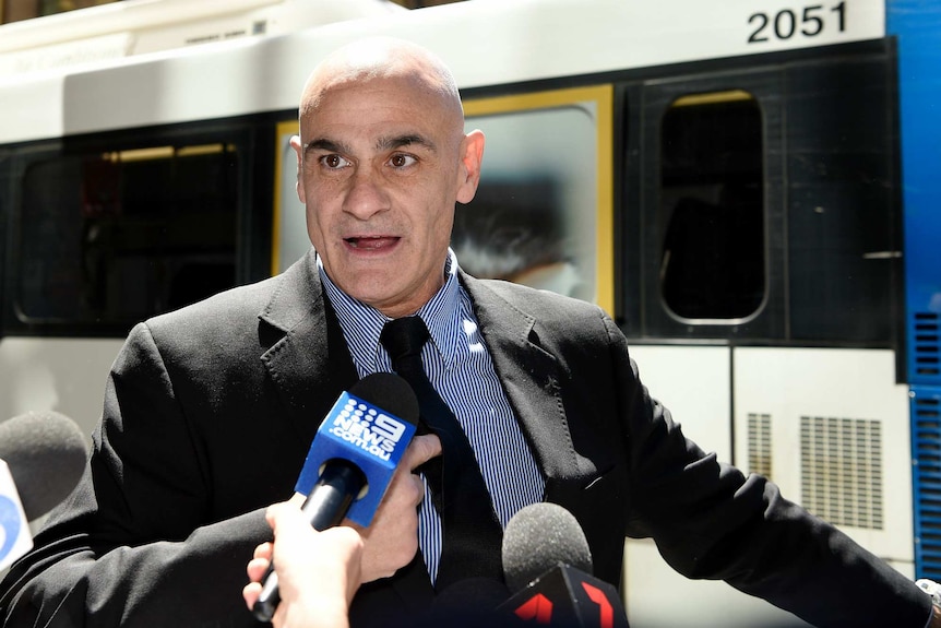 A man speaks in front of media microphones.