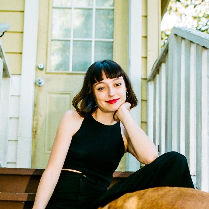 The musician Stella Donnelly sitting out the front of a house, with a dog