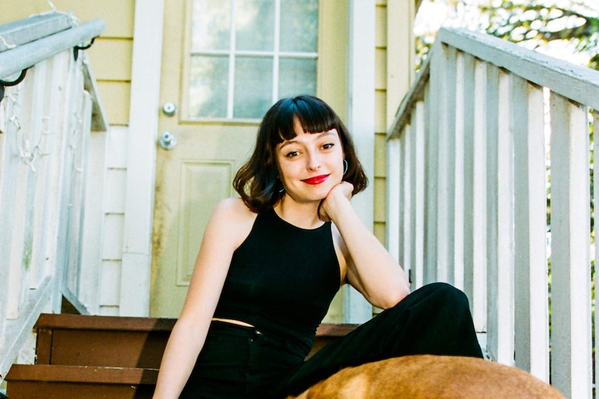 The musician Stella Donnelly sitting out the front of a house, with a dog