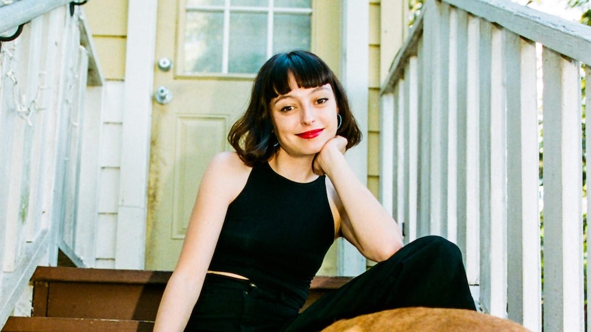 The musician Stella Donnelly sitting out the front of a house, with a dog