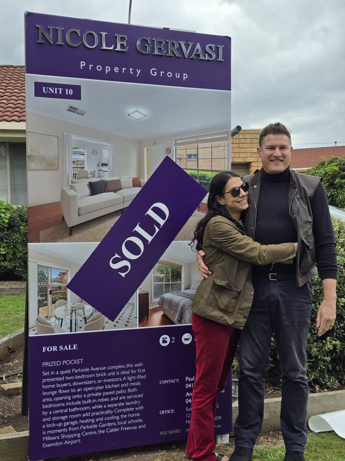 A man and woman standing next to a 'sold' sign in front of their new home.