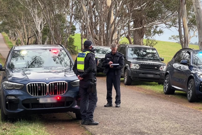 Uniformed officers stand around police cars on a rural road.