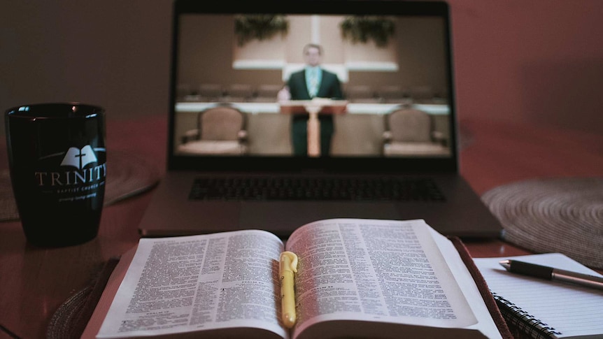 Bible opened in front of a computer that shows a preacher standing in front of a pulpit.