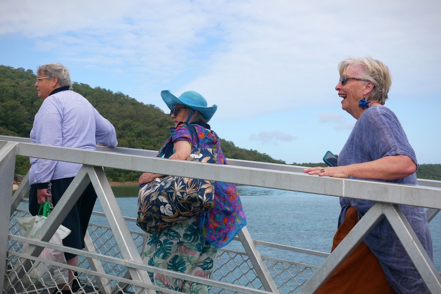 A man followed by two women cross a bridge onto an island