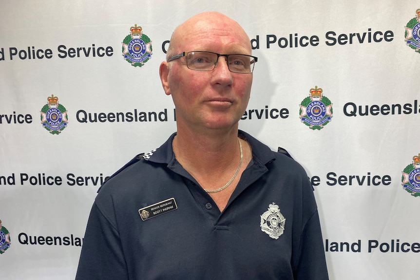 A police officer stands in front of the Queensland Police Service logo