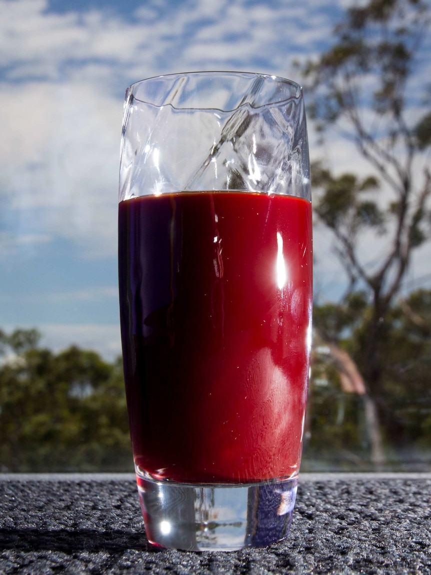 A glass of beetroot juice sits on the floor in front of a window.