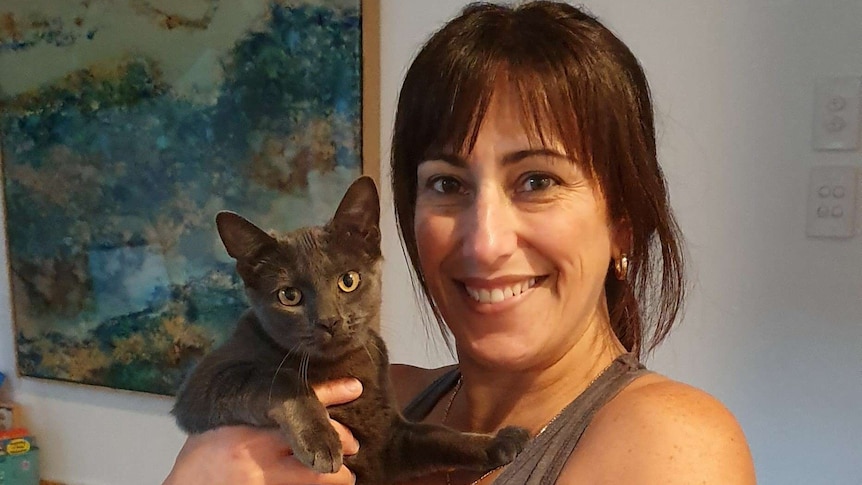 Carmen holds a cat while standing in front of a painting.