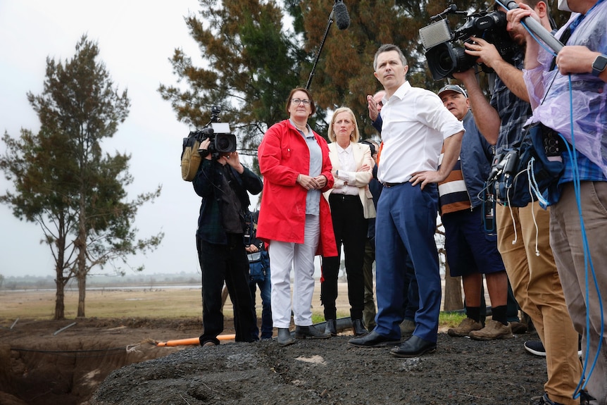 a group of people stand in some dirt surrounded by media