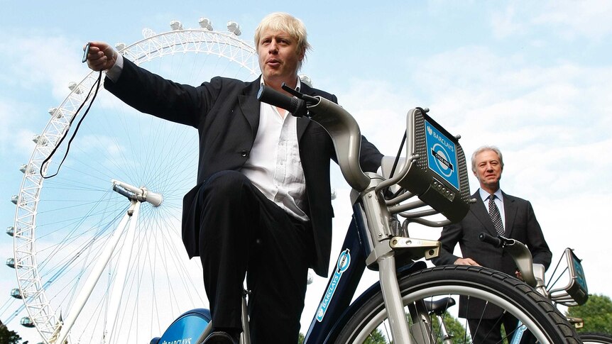 Looking up, Boris Johnson poses on a London share bike with the London eye behind him.