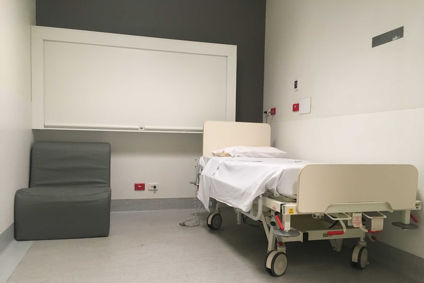 A secure hospital room in the Royal Melbourne Hospital with a bed and chair and roll-down medicine cabinet.