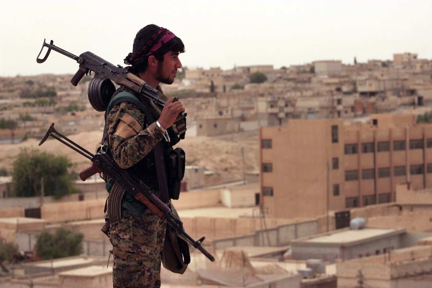 A fighter from the SDF carries weapons as he looks toward the northern town of Tabqa, Syria