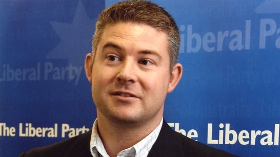 Damien Mantach stands in front of a blue Liberal Party banner