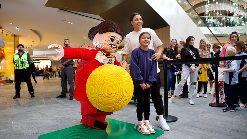 Sam Kerr poses with a LEGO character and a fan in a shopping centre