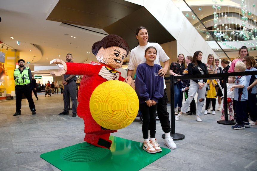 Sam Kerr poses with a toy statue of her and a fan in a shopping centre