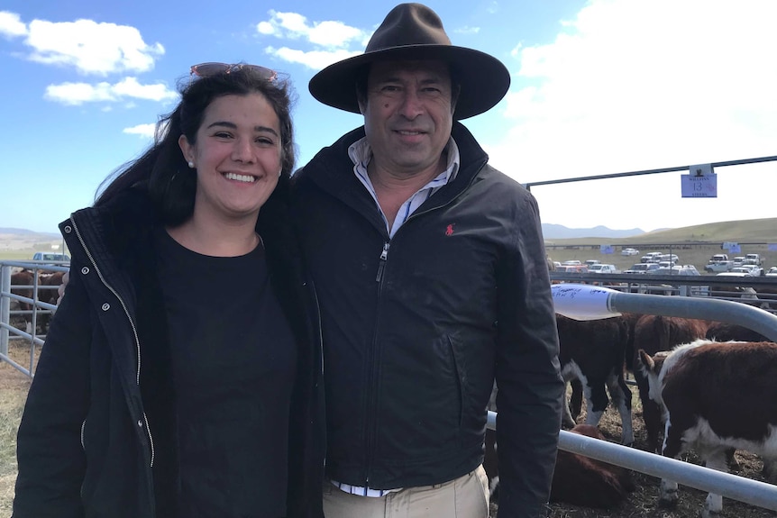 A woman and man stand in front of penned cattle.