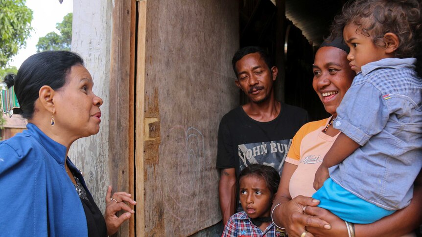 Woman speaks to a man and a woman with their two small children in a doorway.