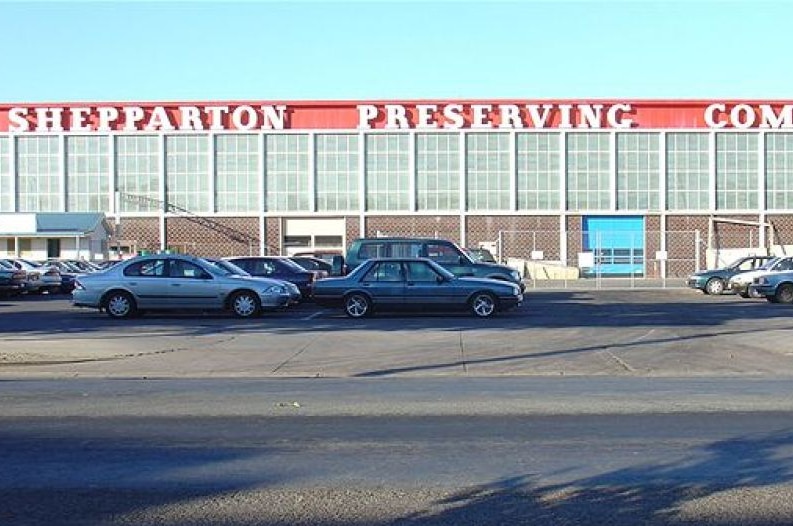 Cars parked out the front of a factory, which has 'Shepparton Preserving Company' in white writing on a red background.