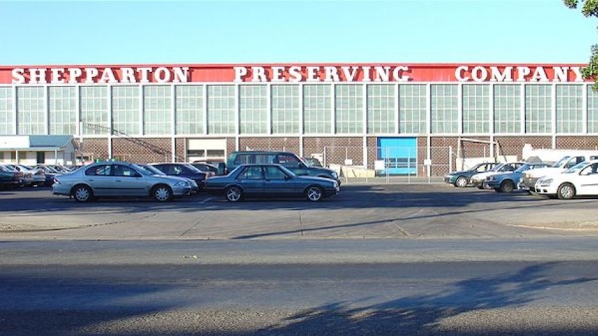 Cars parked out the front of a factory, which has 'Shepparton Preserving Company' in white writing on a red background.