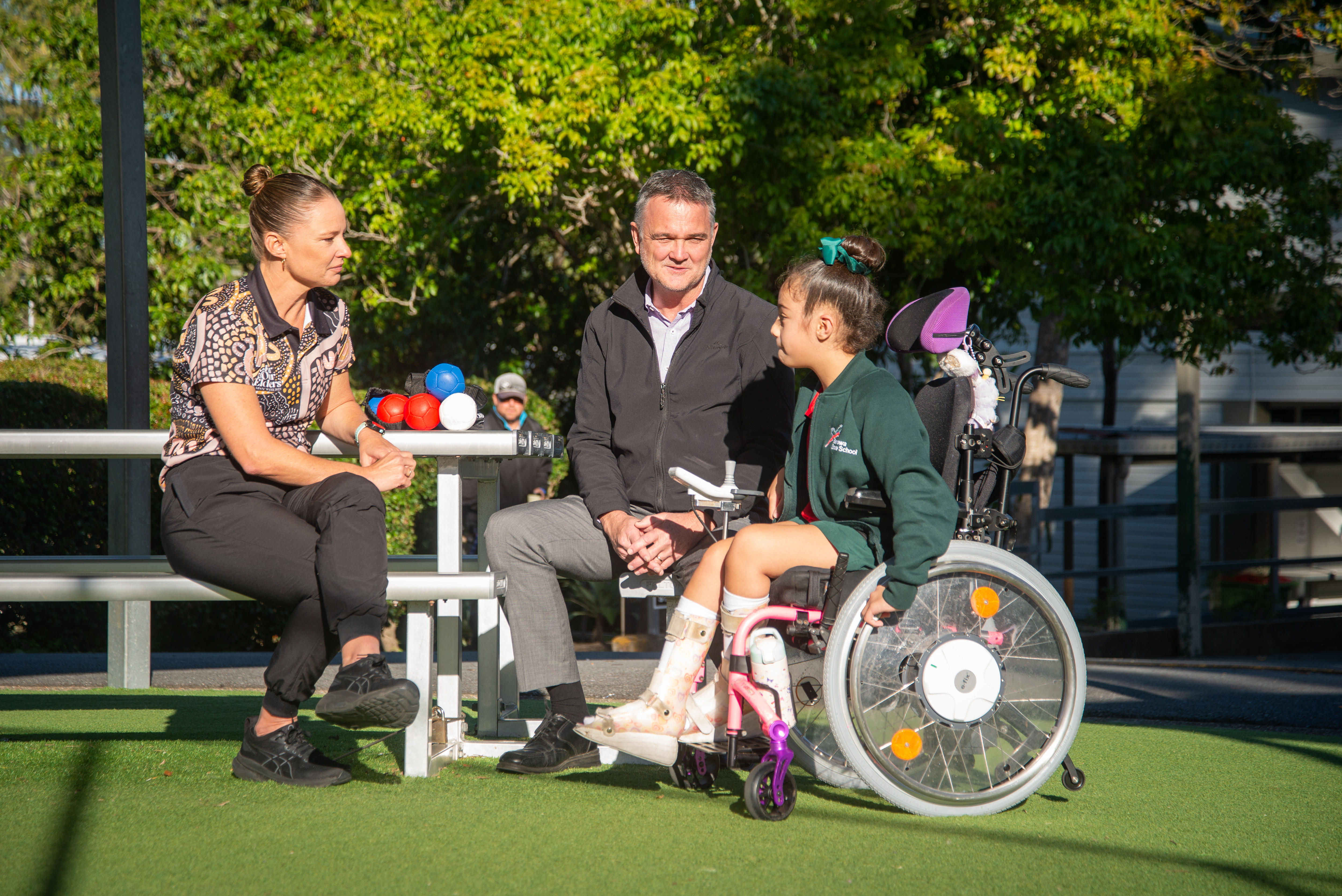 Three people in a small grassed area with a table and chairs.