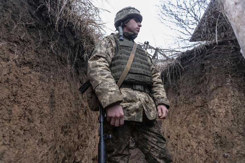 A soldier in camoflague stands in a trench