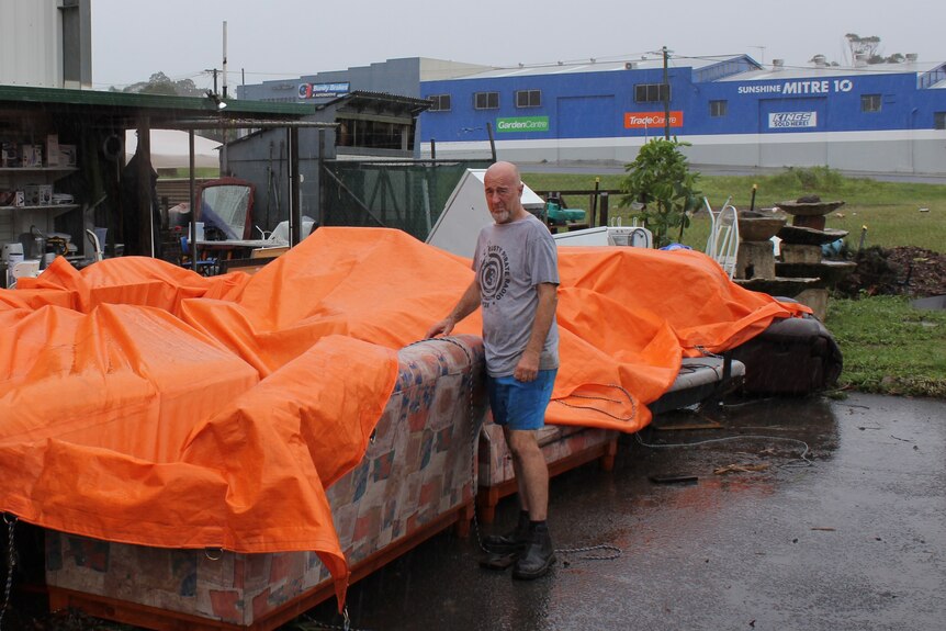 A man stands in the rain with a tarp over his furniture