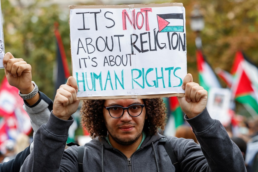 A man holds up a sign saying IT'S NOT ABOUT RELIGION IT'S ABOUT HUMAN RIGHTS