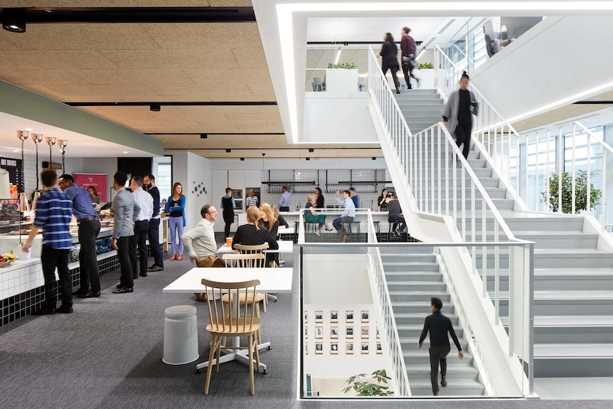 People wait in line at a cafe, while others sit at tables and a woman walks down a central staircase.